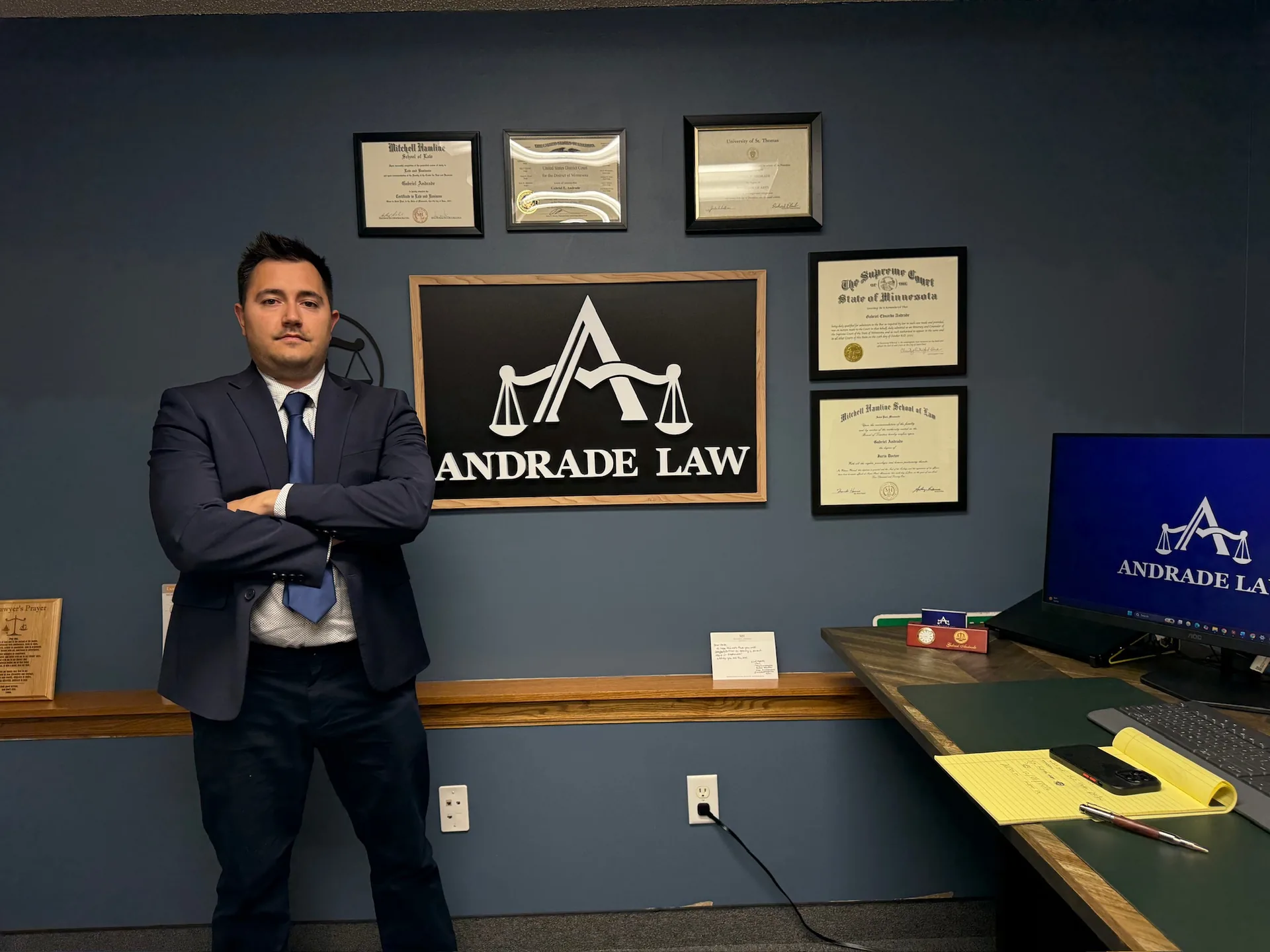 Attorney Gabe Andrade standing in the Andrade Law office in Saint Paul, Minnesota, beside the firm's sign