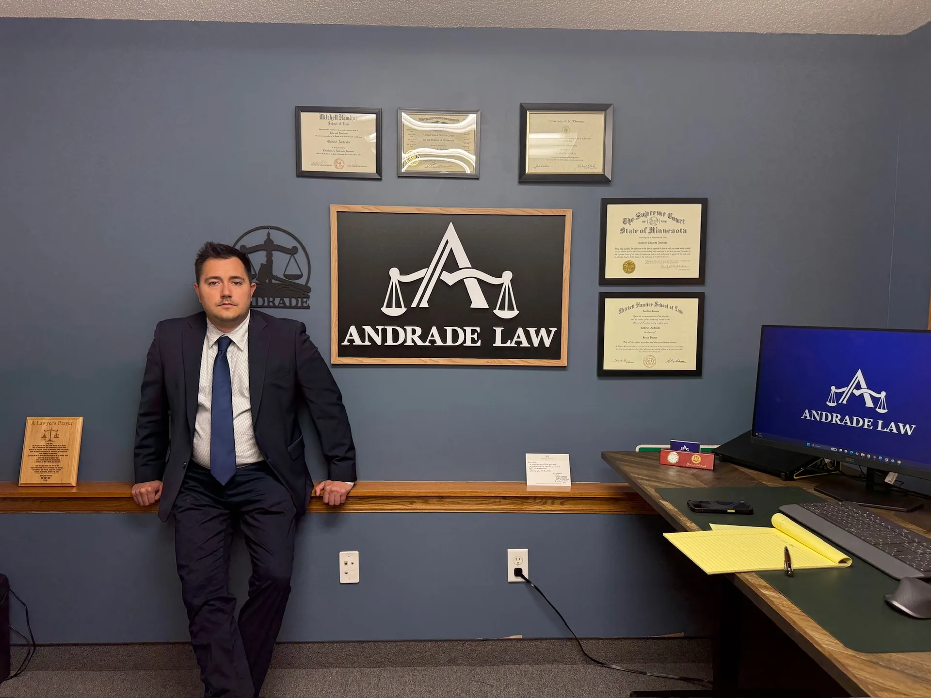 Attorney Gabe Andrade standing at his desk in the Andrade Law office in Saint Paul, Minnesota, by the firm's sign